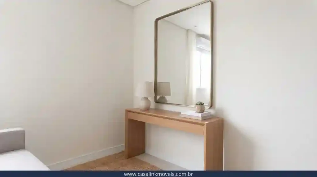 Grande espelho vertical com moldura de latão acima de um aparador de madeira em uma sala pequena, criando profundidade.